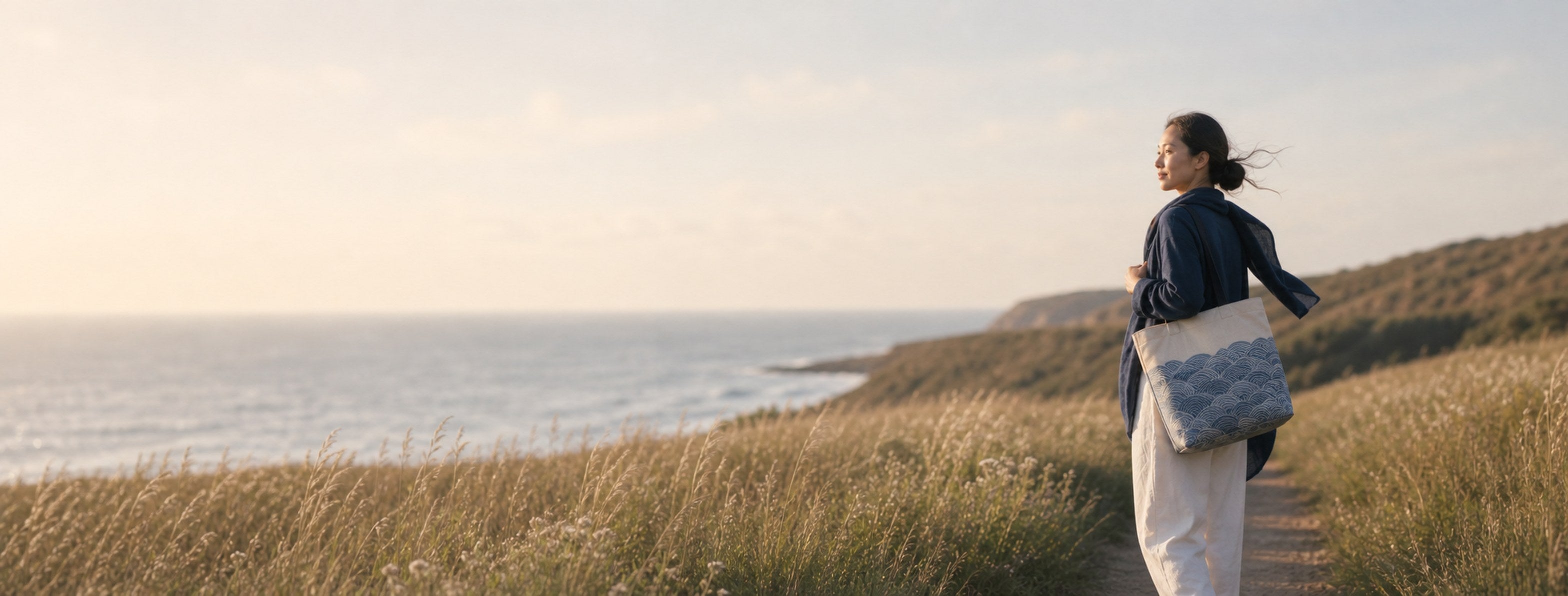 Woman carrying a Chinese Wave Woven Tote on a coastal meadow path